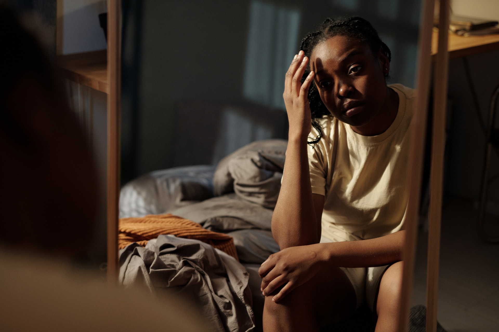 Woman sits alone on the edge of a bed in a dimly lit room